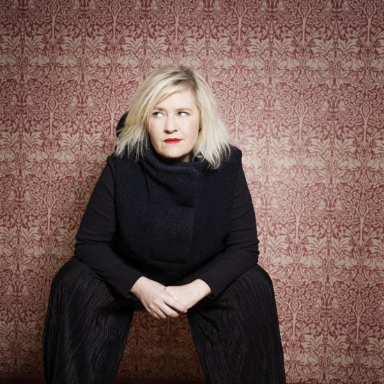 Stine Askov siddende i sort tøj med farverig baggrund