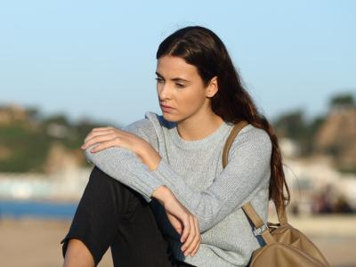 En ung pige sidder på en strand og ser tænksom ud