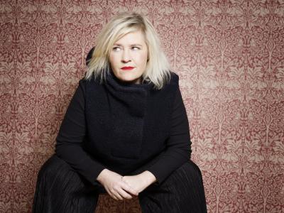 Stine Askov siddende i sort tøj med farverig baggrund