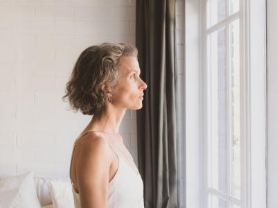 Midaldrende kvinde set i profil kigger ud af vindue