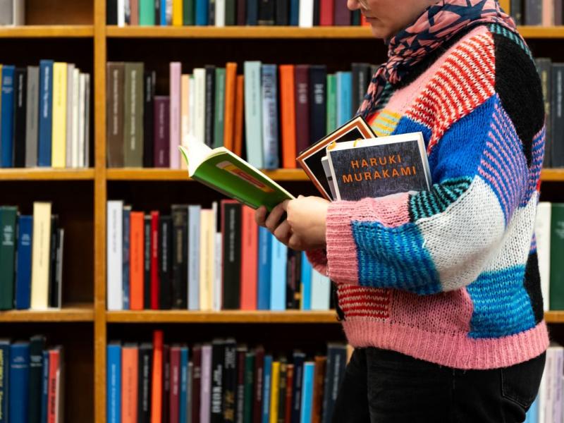 Kvinde med bøger i favnen og en åben bog, hun læser i